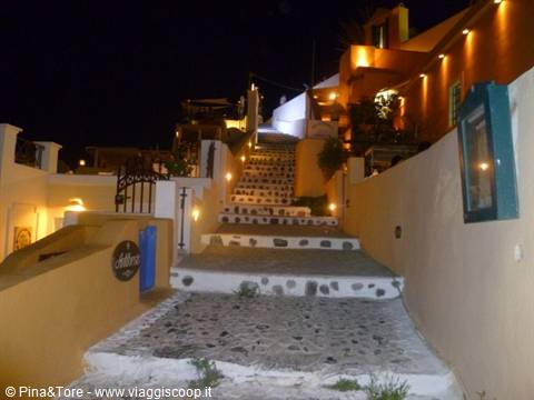 Illuminated stone stairway between white and ochre houses at night, Oia
