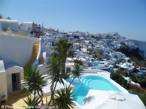 White houses and turquoise pool among palm trees in Imerovigli, clear sky