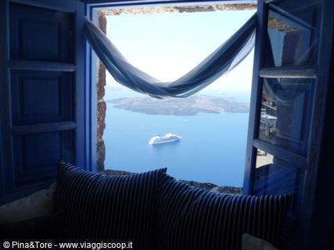 Blue window with curtain framing the caldera and a cruise ship in Oia