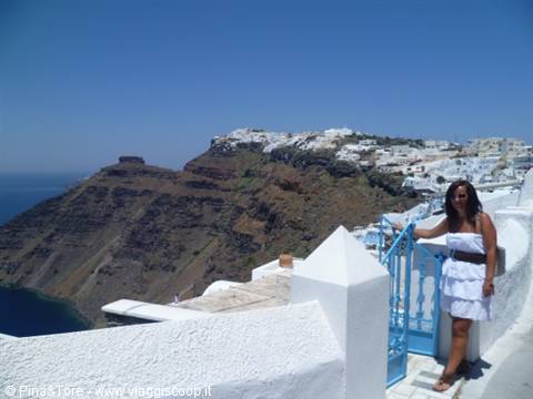 Woman in white dress beside blue gate on white terrace, Fira