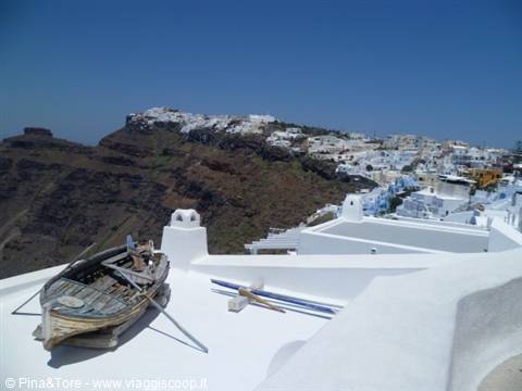 Old wooden boat on white terrace in Firostefani, houses on the caldera cliff