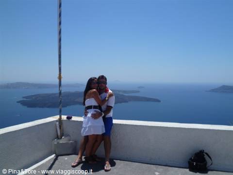 Couple hugging on white terrace in Imerovigli, volcano and Aegean sea behind