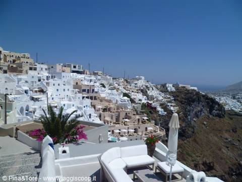 White cave houses on the cliff in Imerovigli, bougainvillea and umbrellas under blue sky