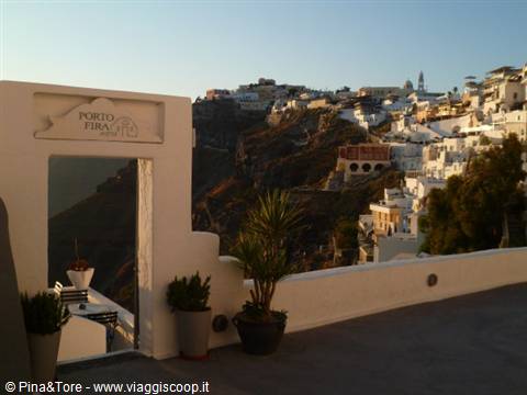 Terrace with Porto Fira sign, potted plants and white houses on Fira caldera
