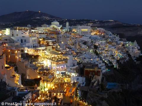 White houses of Thira glowing at night with golden lights on the cliff