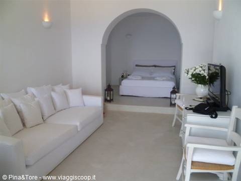 White Cycladic-style room with sofa, bed and warm lights in Oia