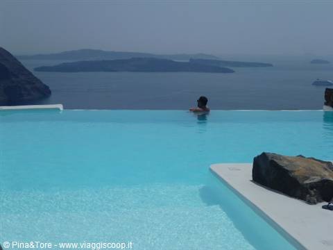 Woman swimming in an infinity pool in Imerovigli, Santorini, volcano in the background