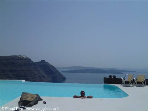 Man relaxing in an infinity pool at Imerovigli, white rooftops over the Aegean Sea