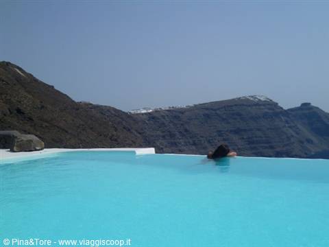 Woman swims in an infinity pool at Imerovigli, volcanic cliffs and white houses behind