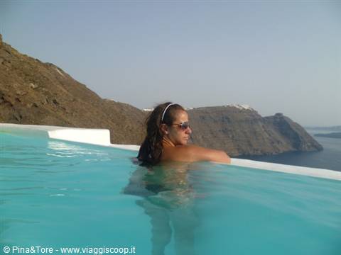 Woman with sunglasses in infinity pool overlooking the Oia caldera