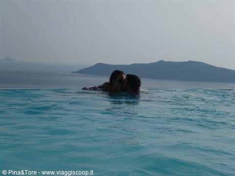 Couple in turquoise infinity pool water facing the caldera, Imerovigli