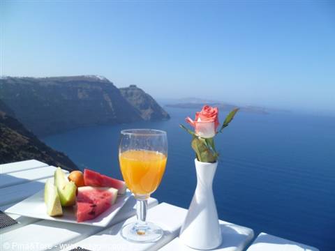 Breakfast with orange juice, fruit and a rose on an Oia terrace