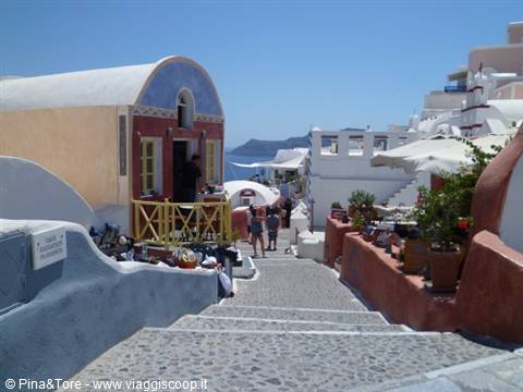 Stone steps between white and ochre houses in Oia, tourists and umbrellas under blue sky