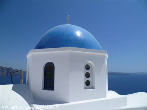 White church with blue dome in Oia, the sea shining under a clear sky