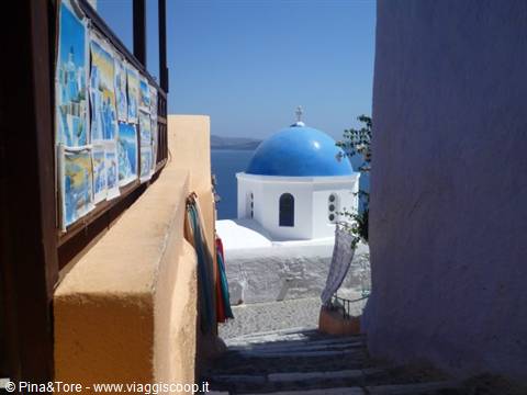 Blue-domed white church among alleys, paintings displayed on Oia steps