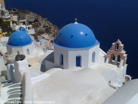 Blue-domed churches and white bell tower in Oia, above the Aegean Sea