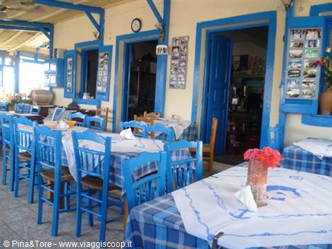 Greek tavern with blue chairs and doors, checkered tablecloths, red flowers in Oia