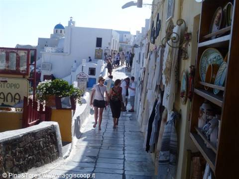 Tourists along Oia's paved alley, pottery shop and white church