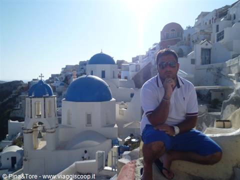 Man sitting beside white churches with blue domes in Oia