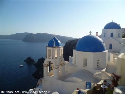 Blue-domed churches above the Oia caldera, bright sun over the Aegean sea