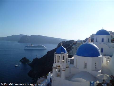 White churches with blue domes in Oia, cruise ship on the caldera sea