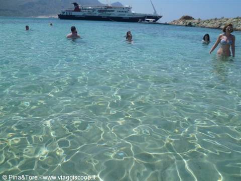 Swimmers in clear turquoise water, ferry anchored near rocks in Crete