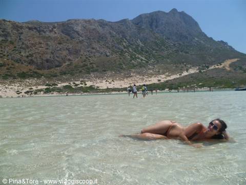 Woman lying in crystal-clear water with tourists and mountains behind, Elafonisi