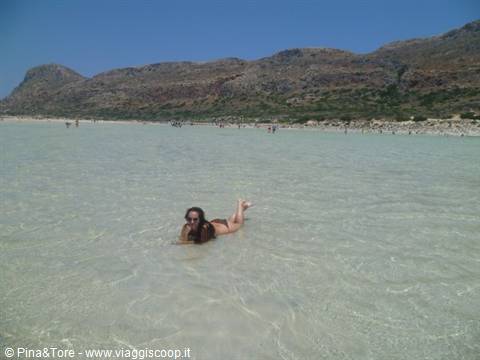 Woman swimming in shallow turquoise water before dunes and mountains, Balos lagoon