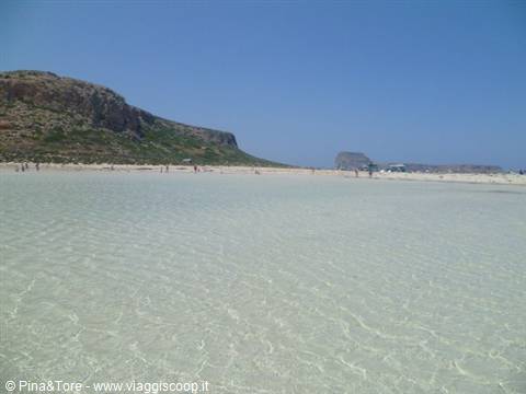 Shallow crystal-clear water of Balos lagoon, with swimmers and rocky hill