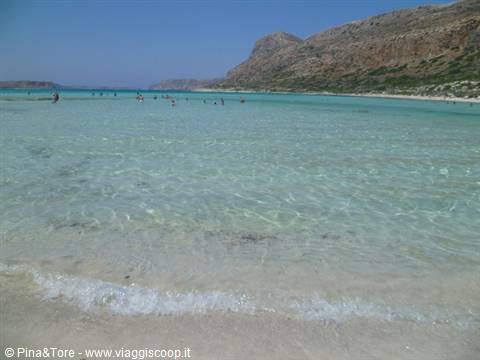 Shallow turquoise water washing over pink sand, swimmers at Balos lagoon