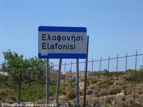 Blue and white Elafonisi road sign among bushes and wire fence