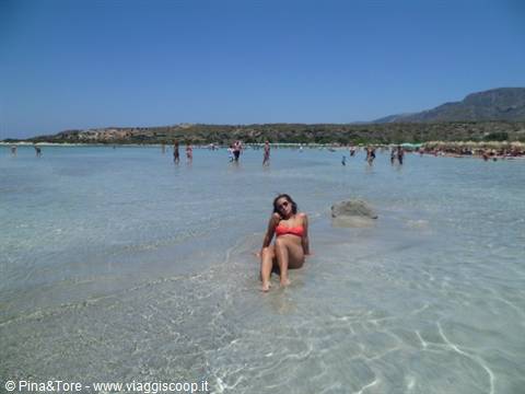 Woman in red bikini sitting in shallow turquoise water, Elafonissi beach