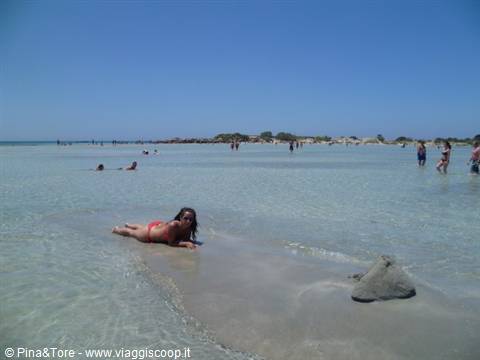Woman lying on low rocks in Elafonissi turquoise shallows, swimmers around