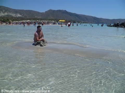 Tourist sitting on a rock in the shallow turquoise water of Elafonissi lagoon