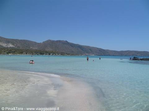 Turquoise shallow lagoon at Elafonisi, swimmers on pale sand beneath mountains