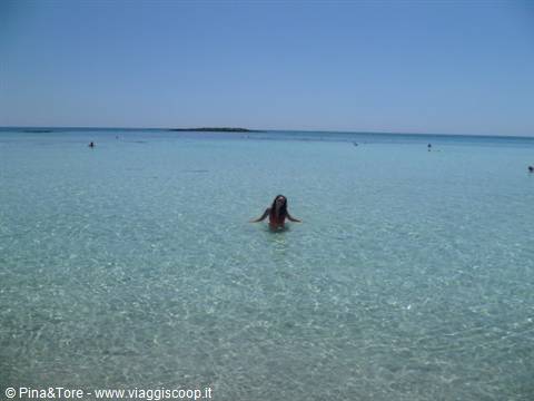 Woman swimming in shallow turquoise sea, sandy beach in Crete