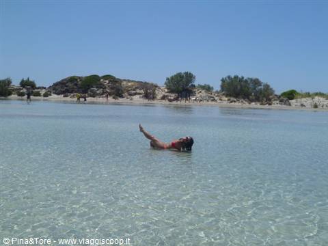 Woman swimming in shallow crystal water in front of a sandy Cretan beach