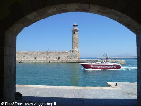 Chania Venetian lighthouse seen through a stone arch, a parasailing motorboat passing by
