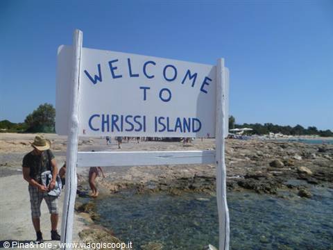 White wooden Welcome to Chrissi Island sign on a rocky beach