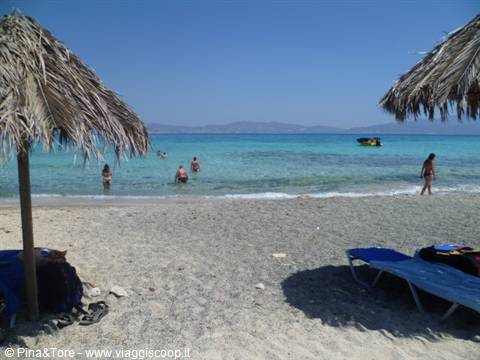 Sandy beach with straw umbrellas and swimmers in turquoise water