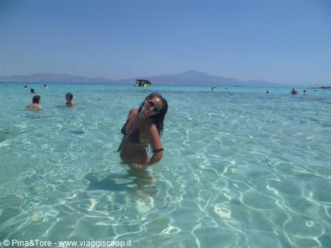 Woman in bikini smiling in shallow turquoise water, swimmers and mountains behind
