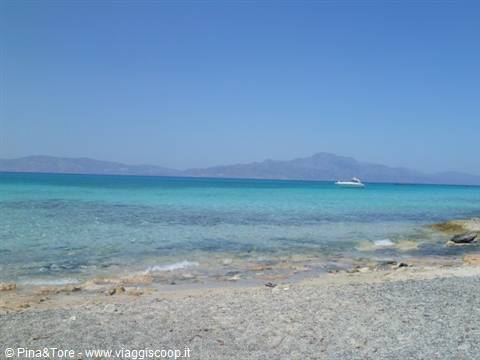 Pebbly beach with turquoise sea and a white boat, Cretan coast under blue sky