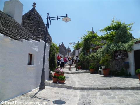 Tourists walk among Alberobello trulli, whitewashed walls and stone conical roofs