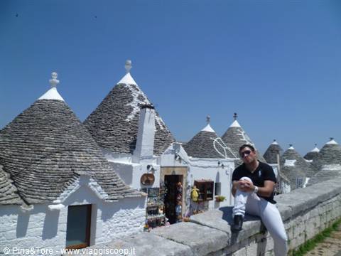 Tourist sitting on a low wall in front of Alberobello's stone trulli houses
