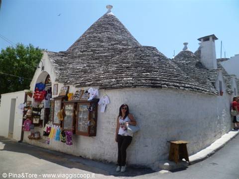 Tourist in front of an Alberobello trullo with stone roof and souvenirs