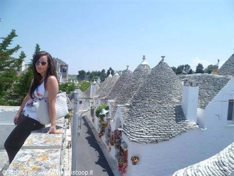 Girl sitting on a wall in front of Alberobello trulli, conical stone roofs