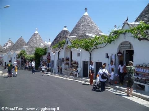 Tourists among Alberobello trulli, white stone houses with conical roofs in sunlight