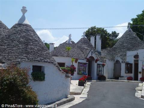 Trulli houses in Alberobello with stone cone roofs and flowers under sun
