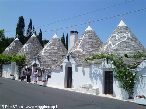 Trulli in Alberobello, conical stone roofs with white symbols, tourists under sunny sky