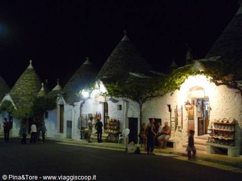 Trulli houses in Alberobello at night, stone cone roofs, tourists under shop lights